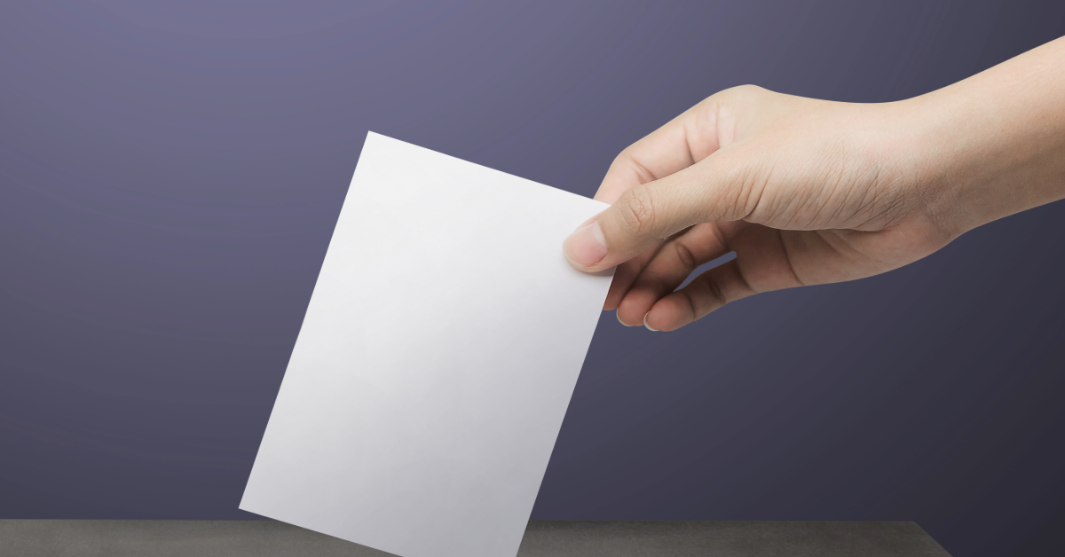 A hand dropping a ballot paper into the ballot box.